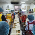 新業(yè)同仁與志工們繫上圍裙、套上防塵帽，戴上口罩，手捧一份份飯包各司其職，為的是準(zhǔn)時(shí)將熱騰騰的飯包送到長(zhǎng)輩手中。